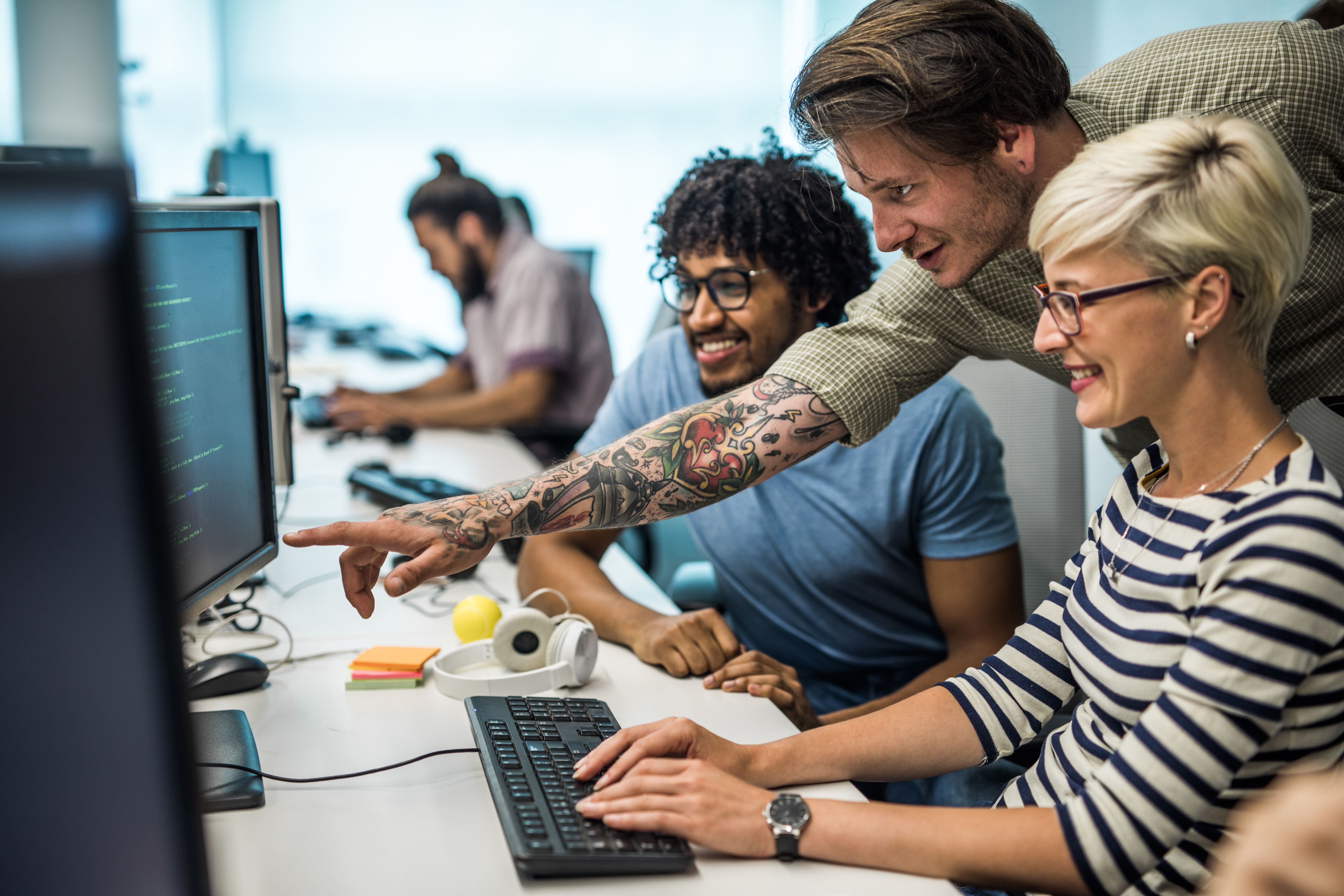 Tre unga personer tittar på en datorskärm på ett kontor.