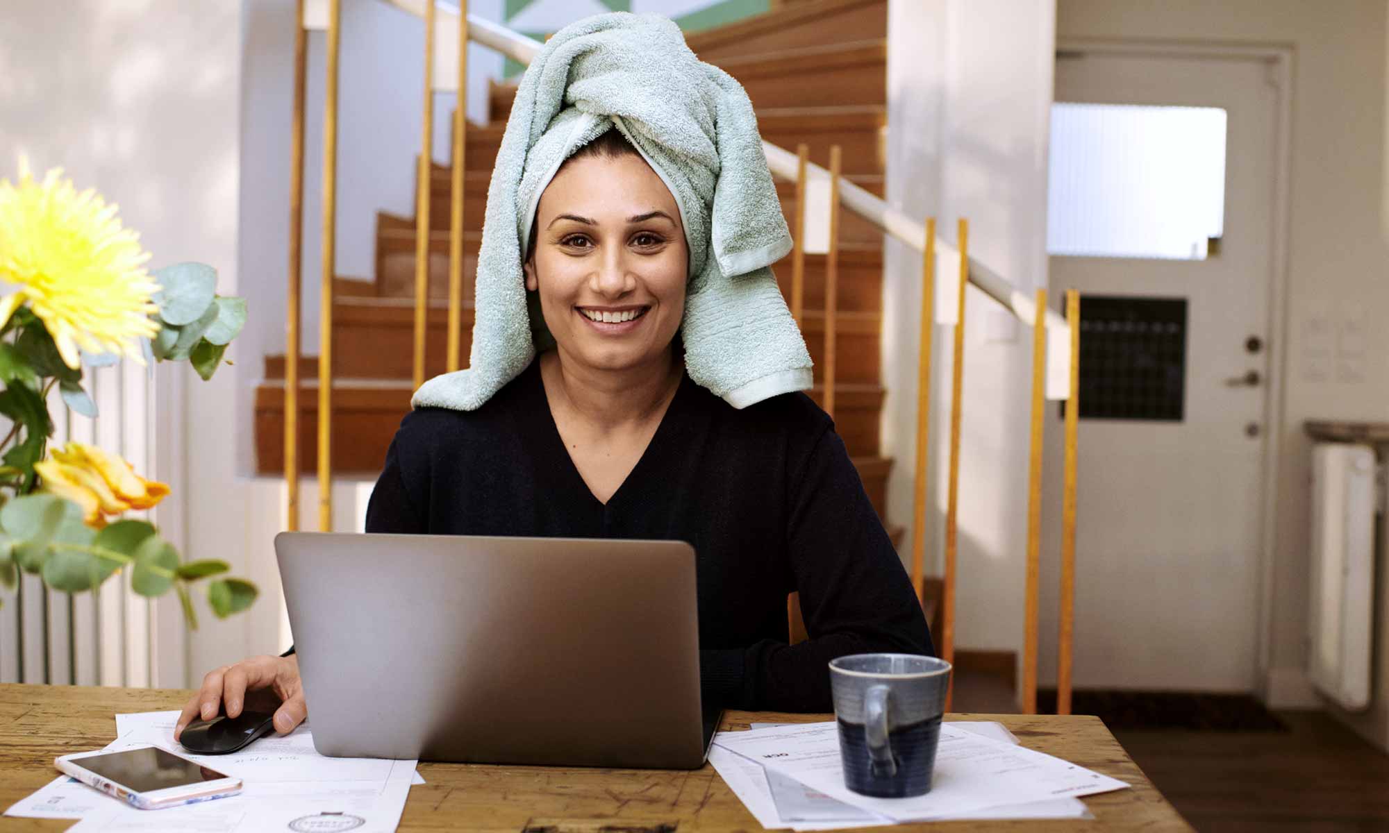 Kvinna med handduk virad runt huvudet sitter och ler framför datorn