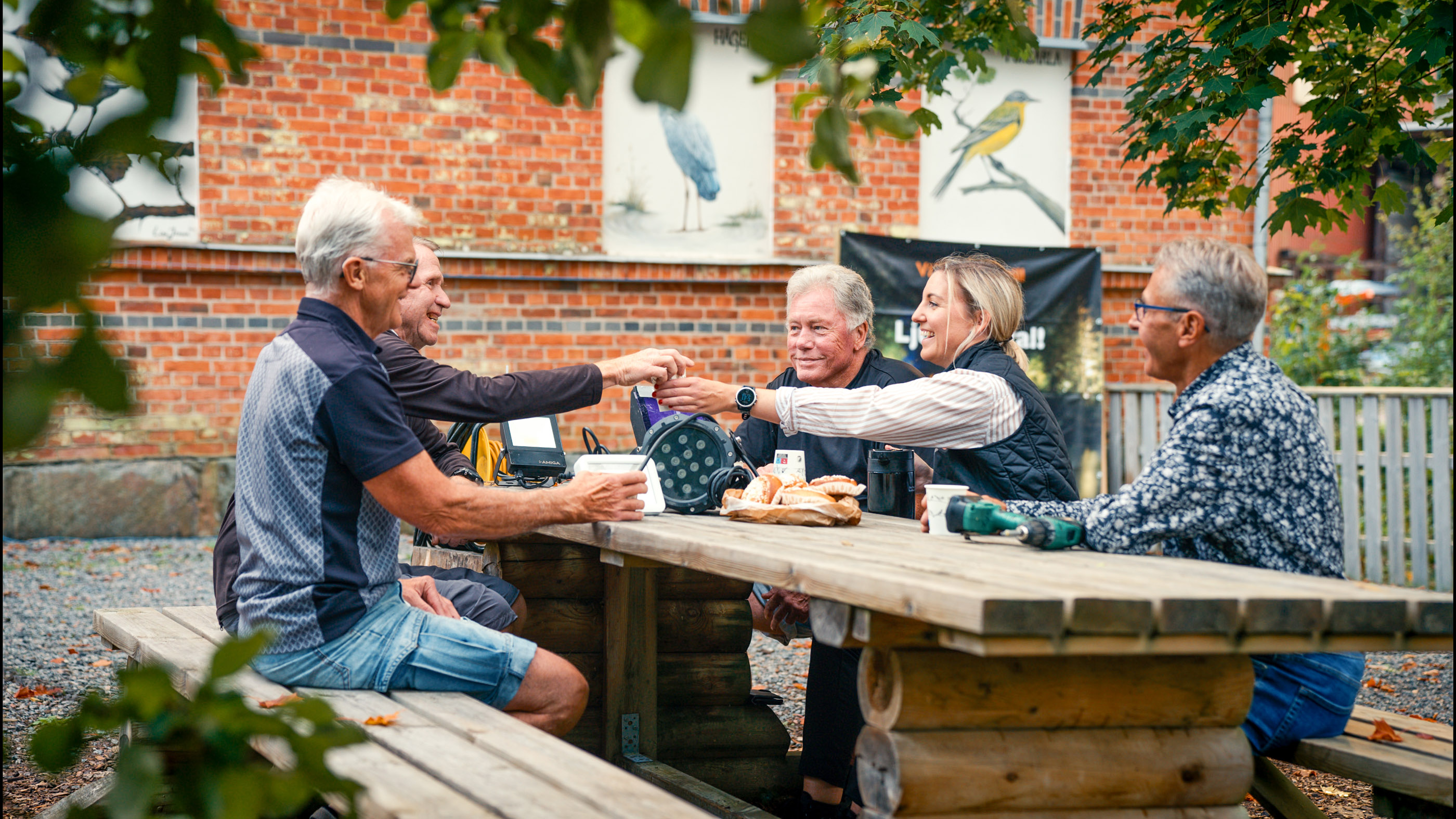 En grupp människor sitter på bänkar och fikar